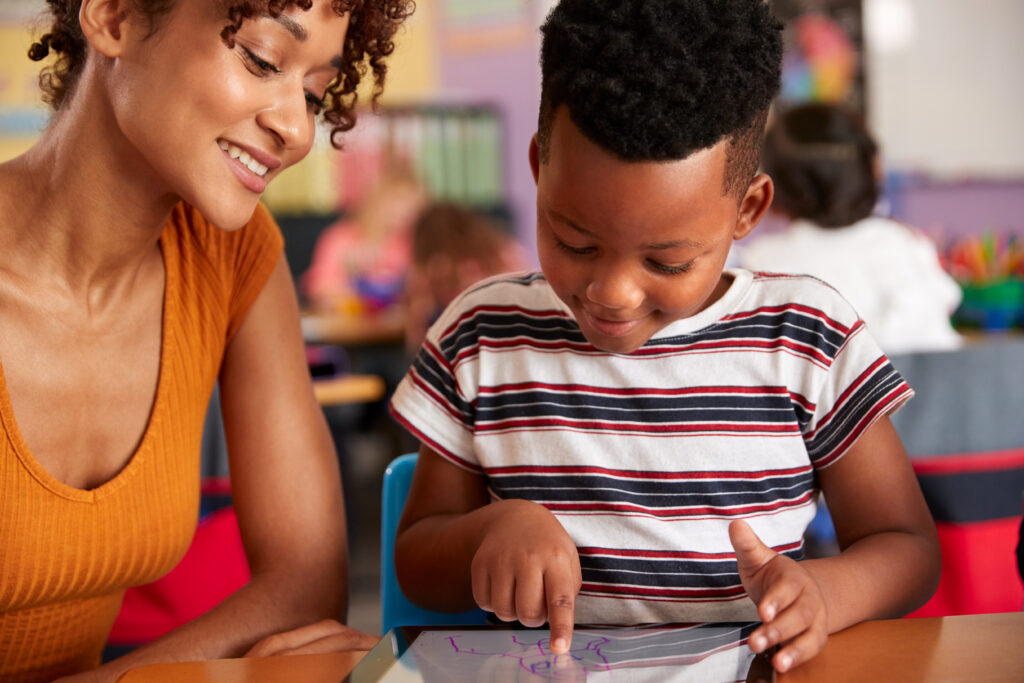 elementary school teacher and male pupil drawing using digital tablet in classroom