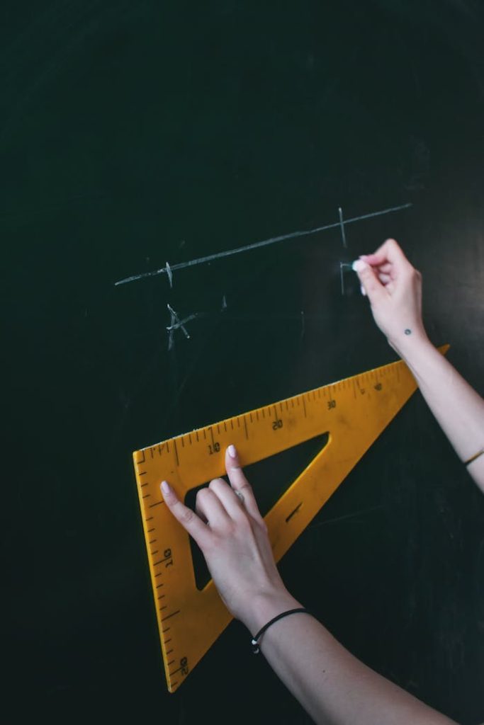 Two hands drawing a line with chalk on a blackboard using a triangle ruler