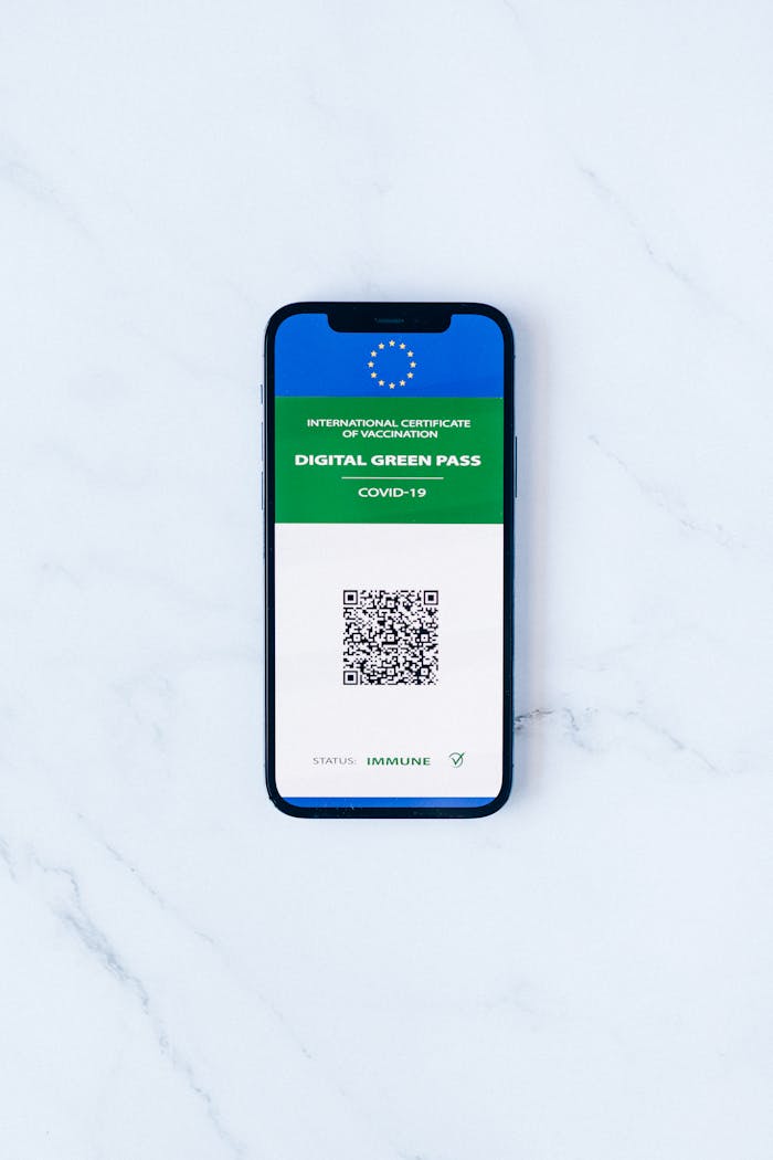 A smartphone displaying a digital green pass with QR code on marble surface.
