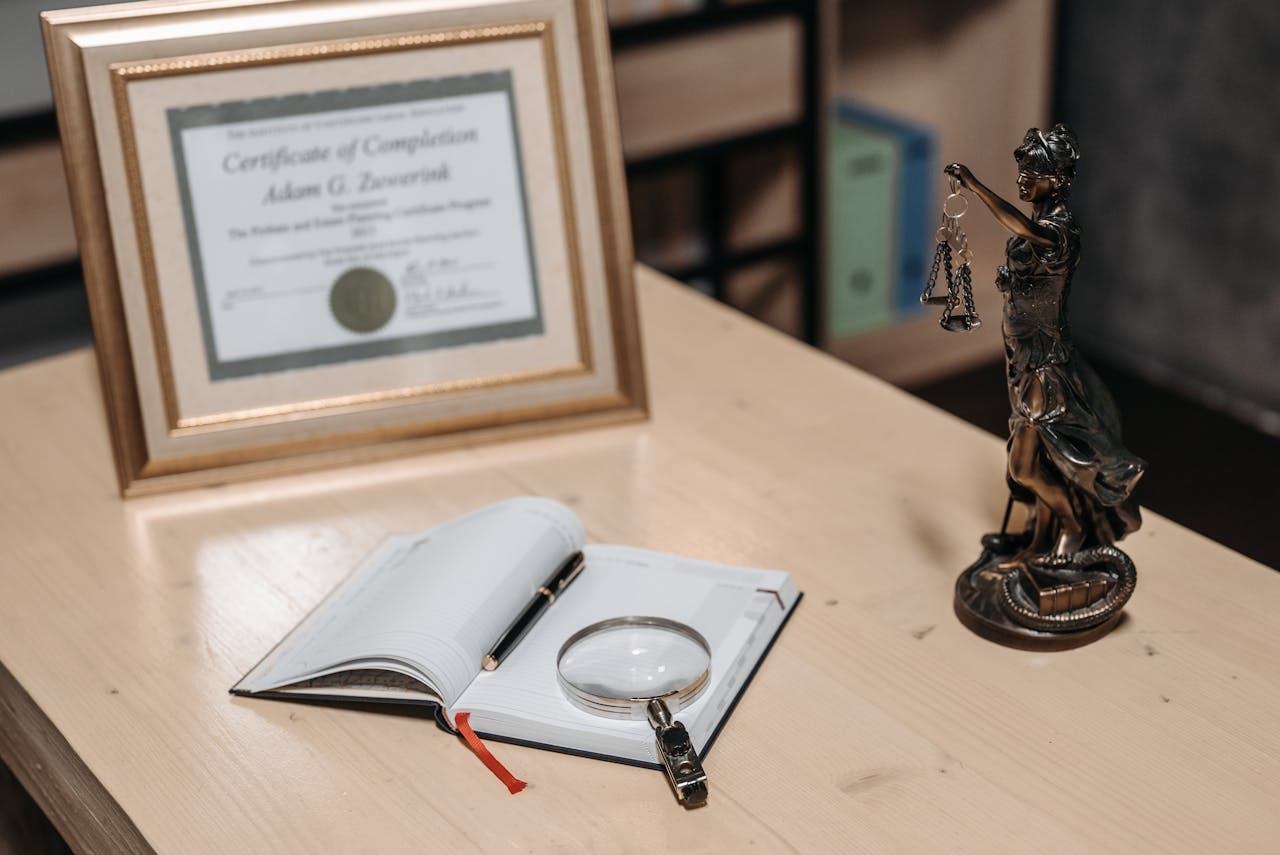 A framed certificate with Lady Justice statue on a wooden desk.