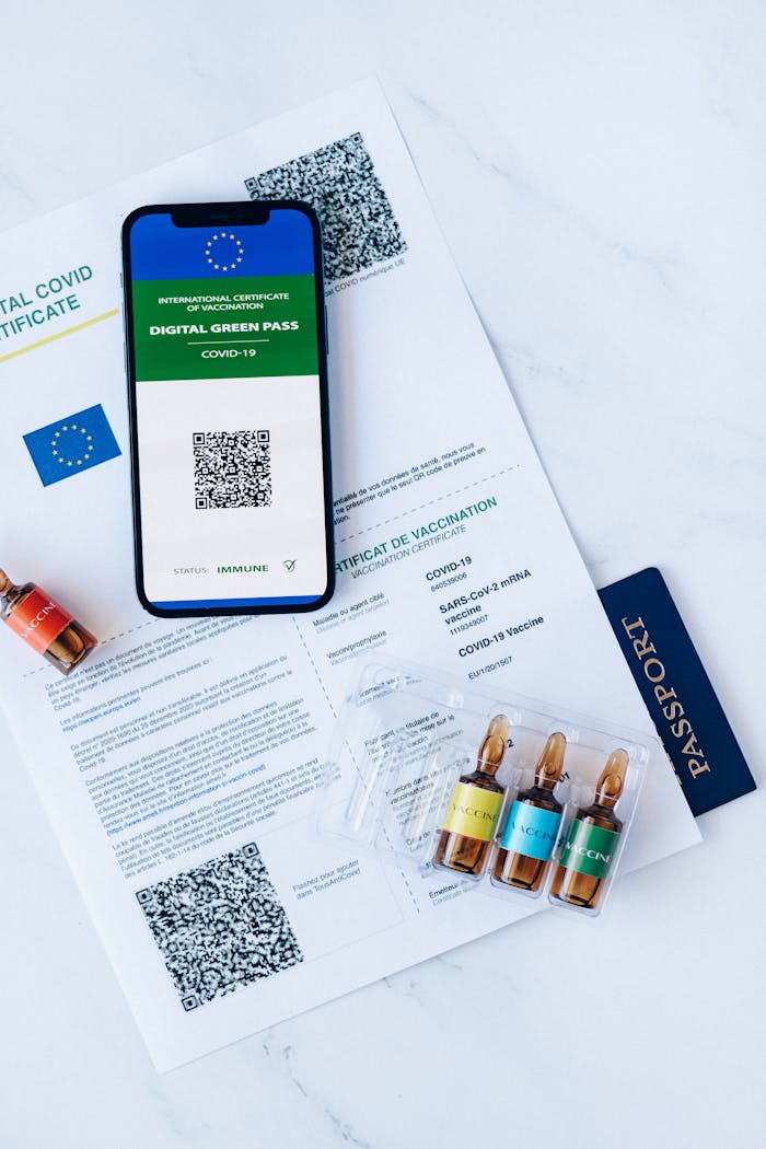 COVID-19 digital green pass with ampoules and EU passport, flat lay on marble.
